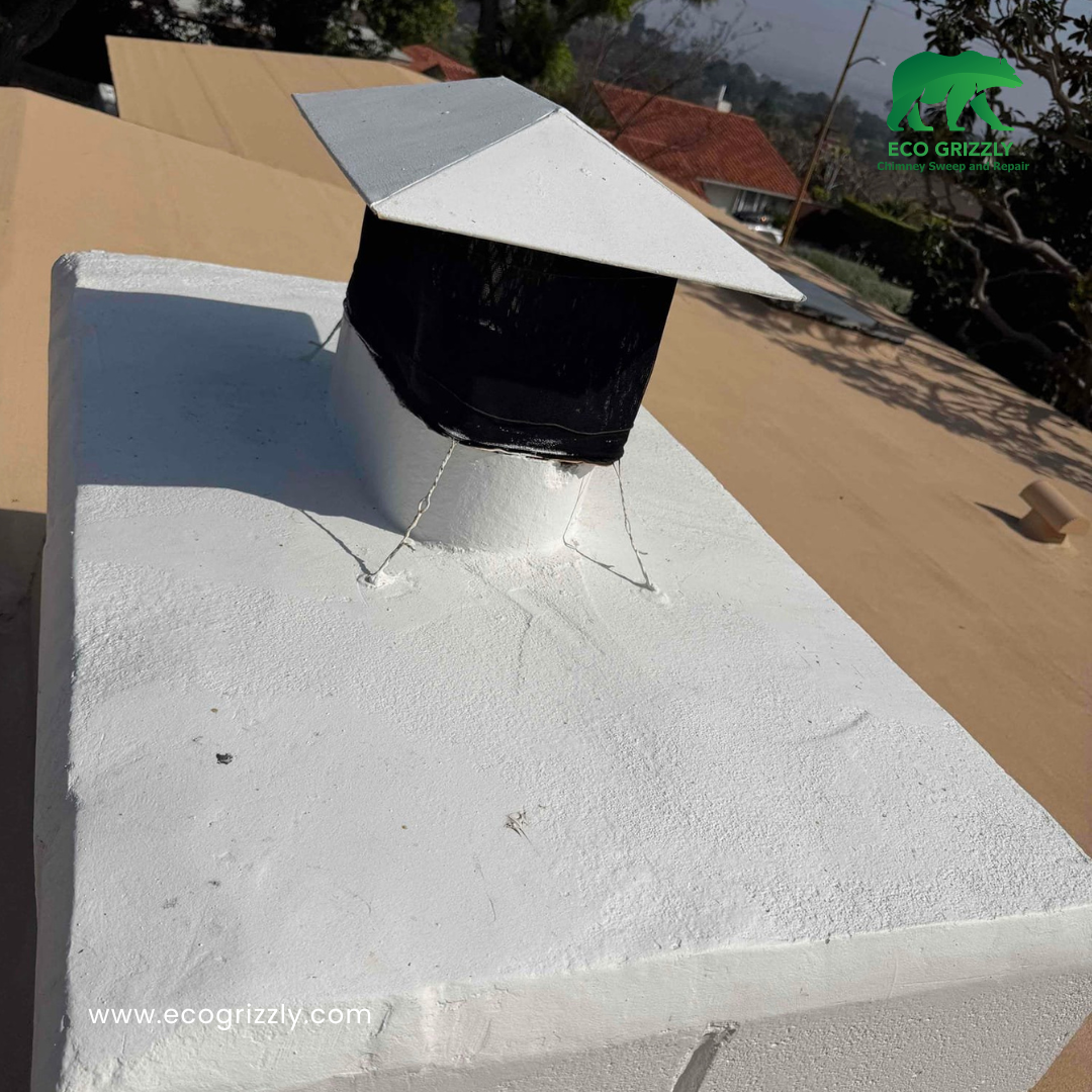 White chimney crown with silver and black chimney cap installed on a tan roof