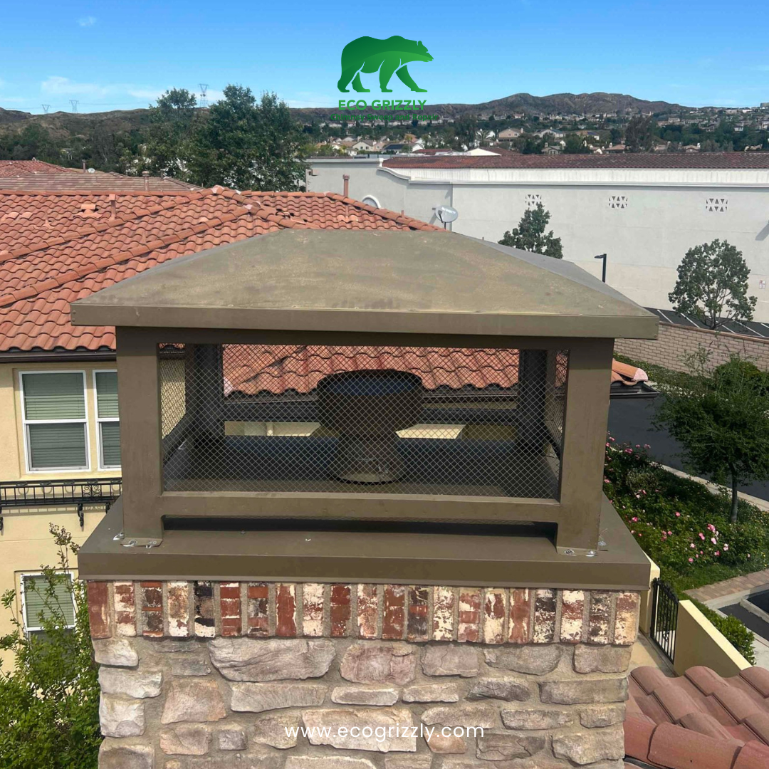 Bronze chimney cap with mesh sides on a stone and brick chimney with hills in background