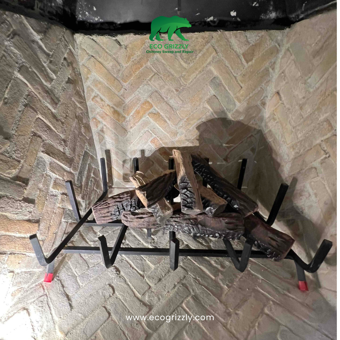 Brick fireplace interior with herringbone pattern and metal grate holding artificial logs
