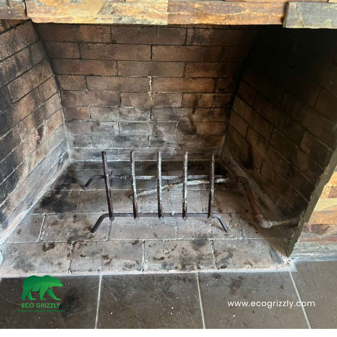 Brick fireplace interior with metal grate and visible soot buildup on hearth and walls