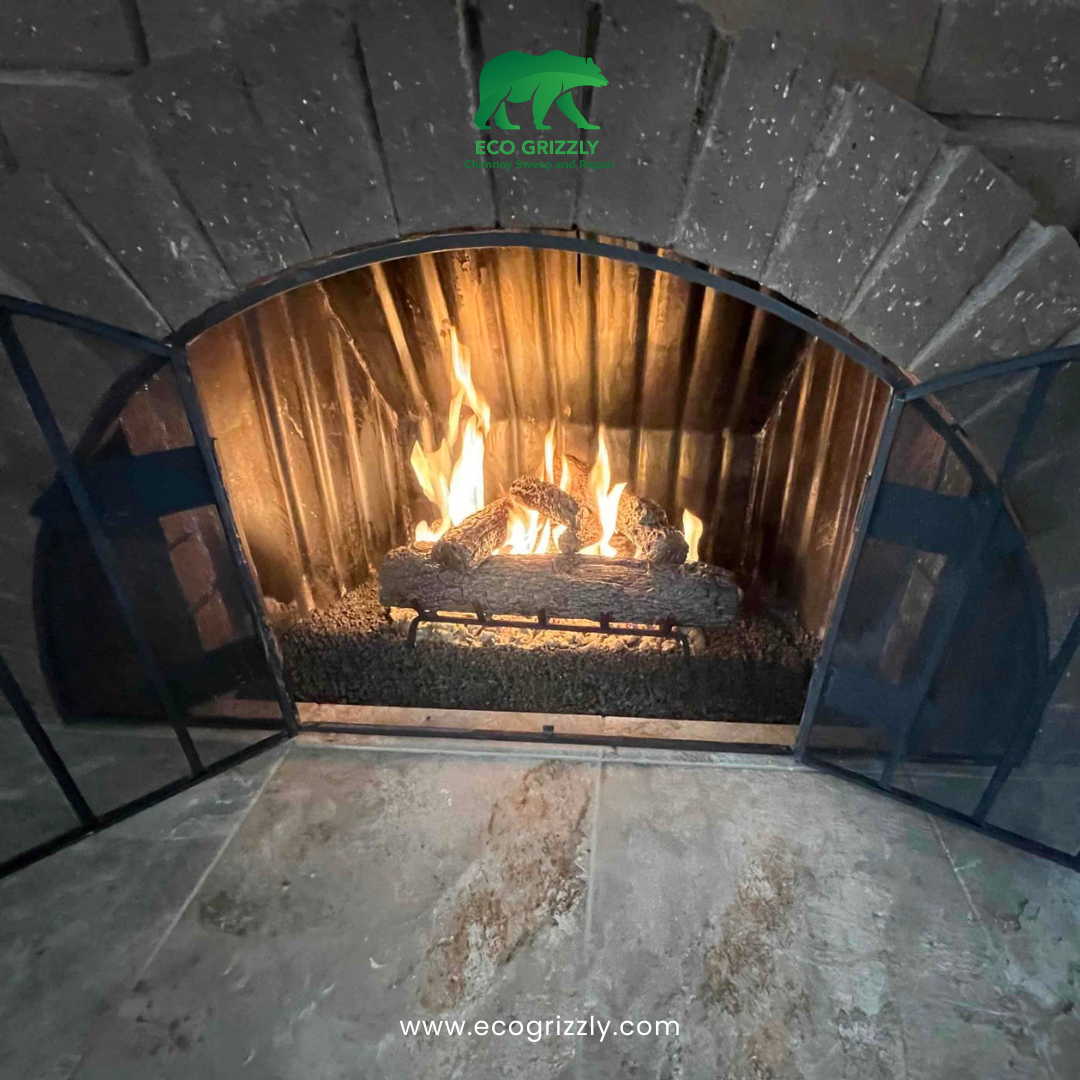 Arched brick fireplace with gas log set burning behind a metal screen